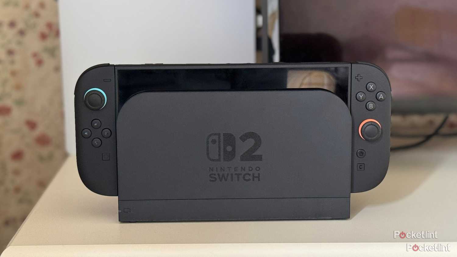 A Nintendo Switch 2 docked with a Playstation 5 and TV in the background.