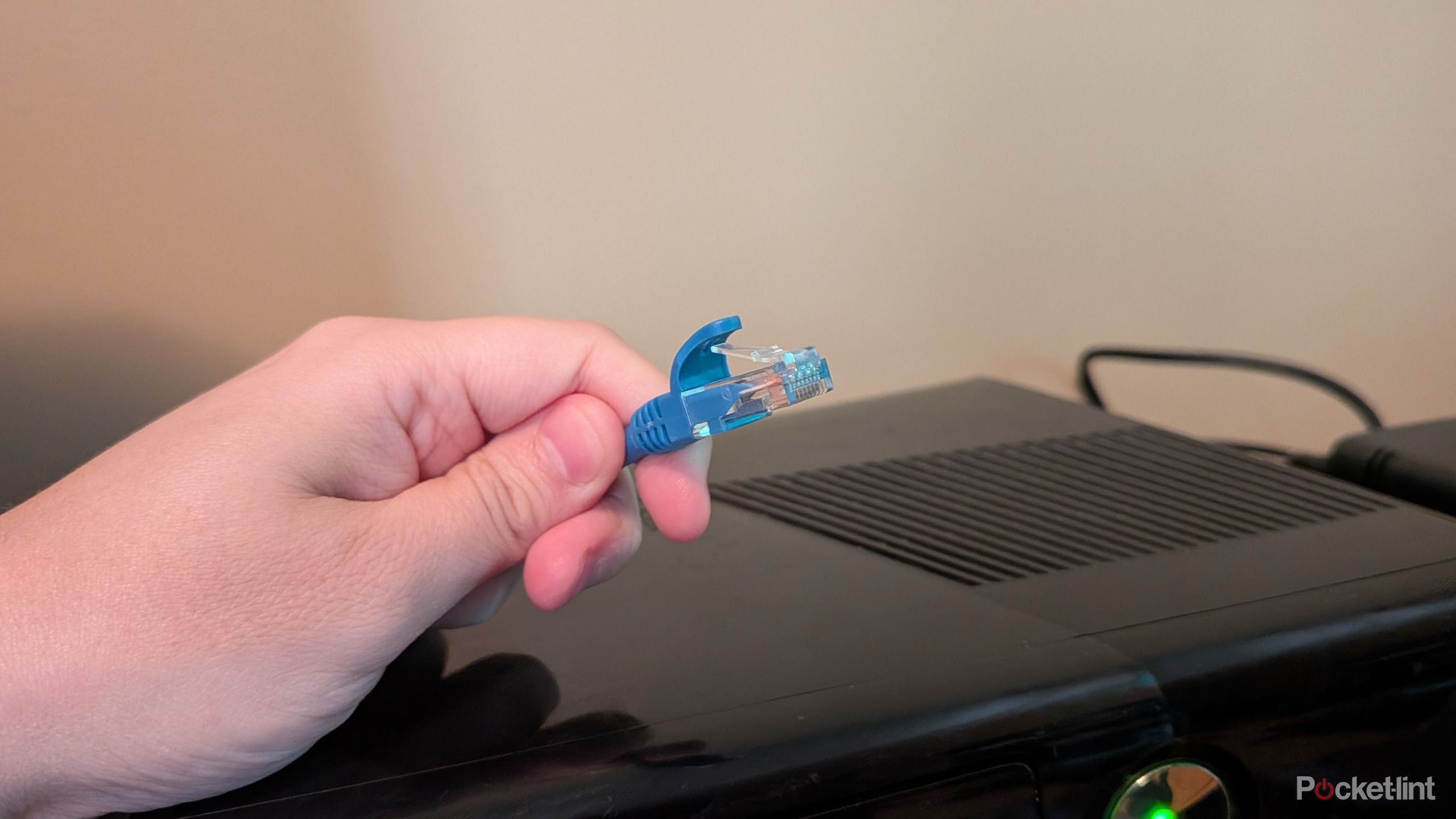 A person holding an Ethernet cable over an Xbox 360.