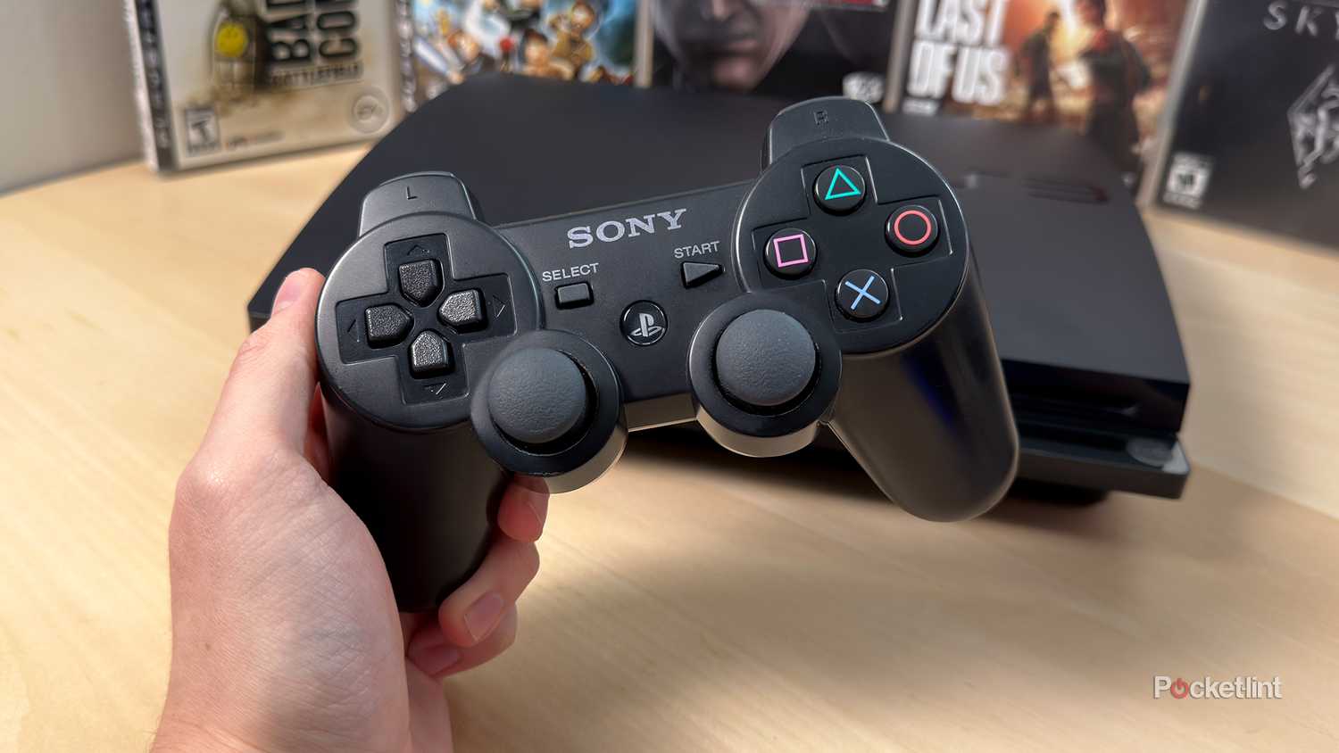 Person holding PS3 controller in front of PS3 console and games.