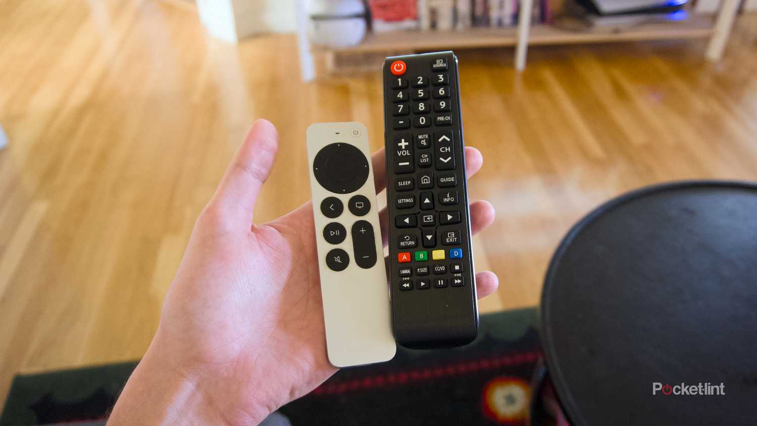 A hand holding a Siri Remote and a Samsung universal remote.