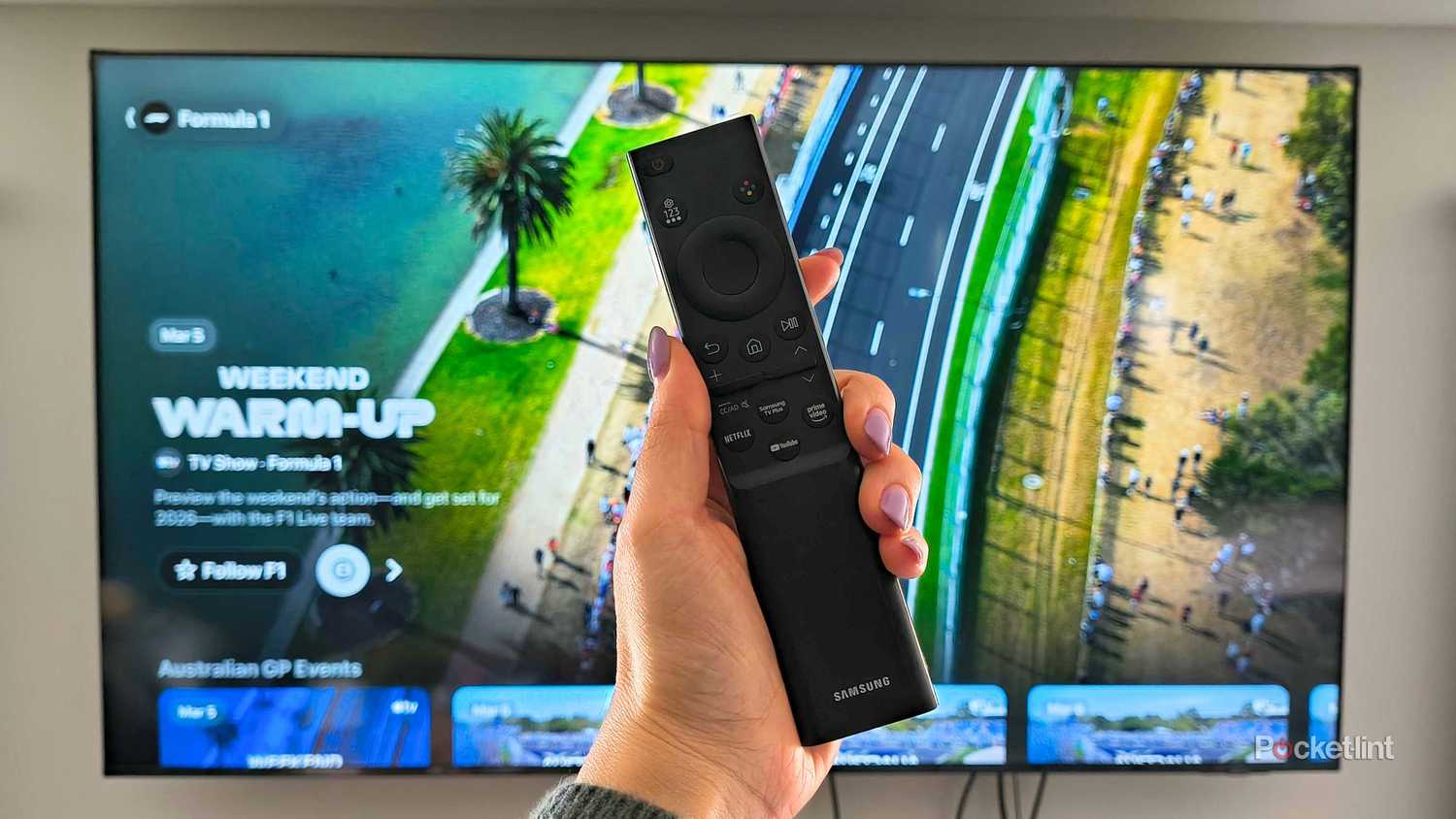 A person holding a remote in front of the Apple TV F1 channel.