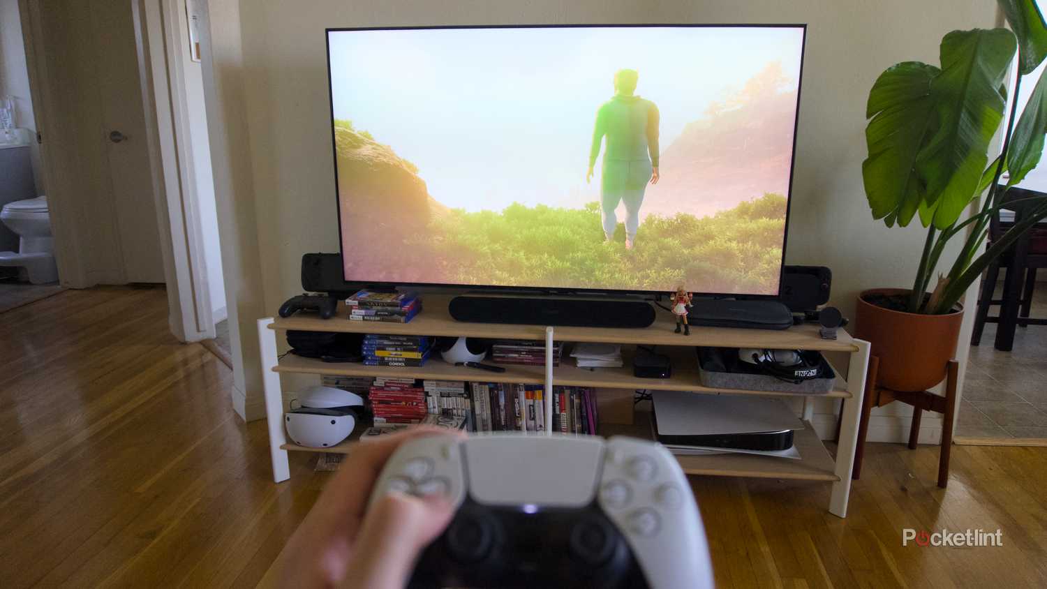 Hands holding a PS5 controller in front a TV displaying the game Baby Steps.