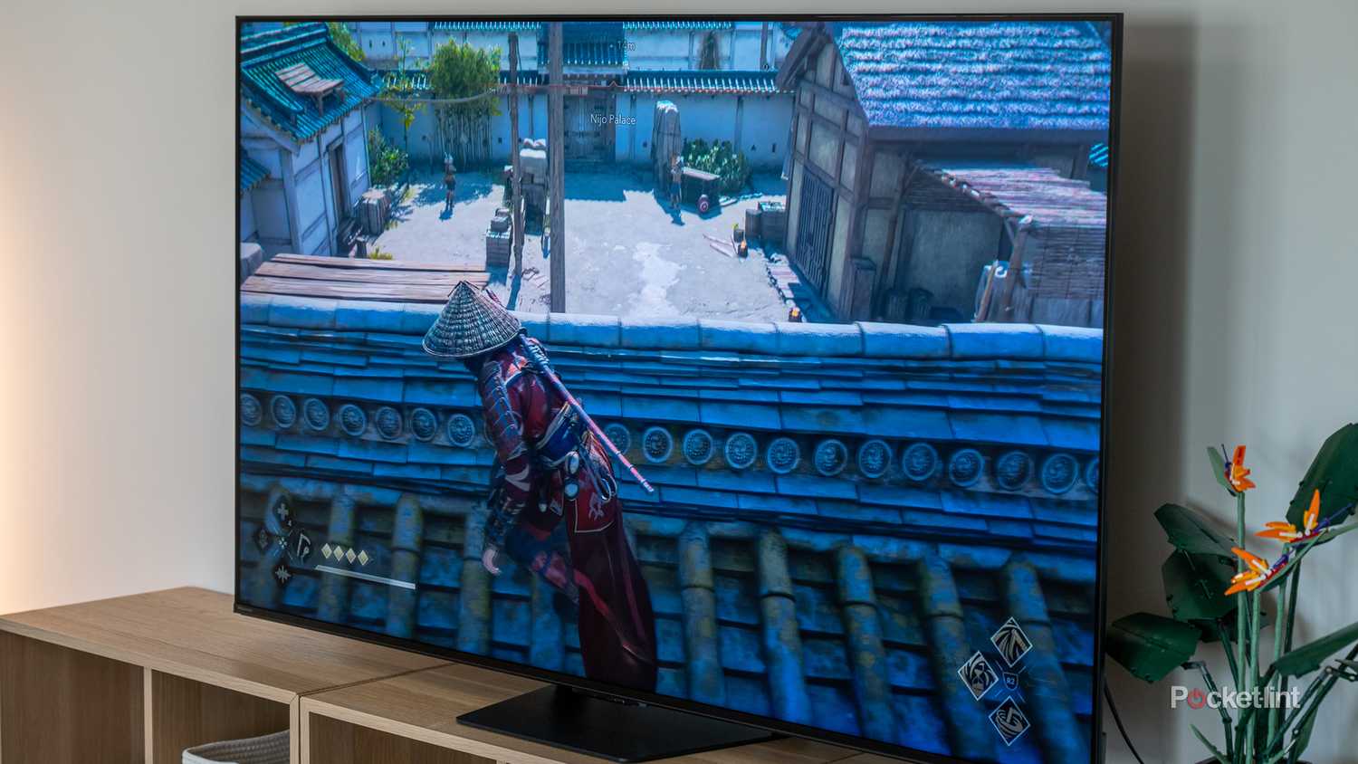 Hisense U7 TV on wood entertainment unit at an angle displaying a video game scene of a samurai crouching on a rooftop in a Japanese courtyard.