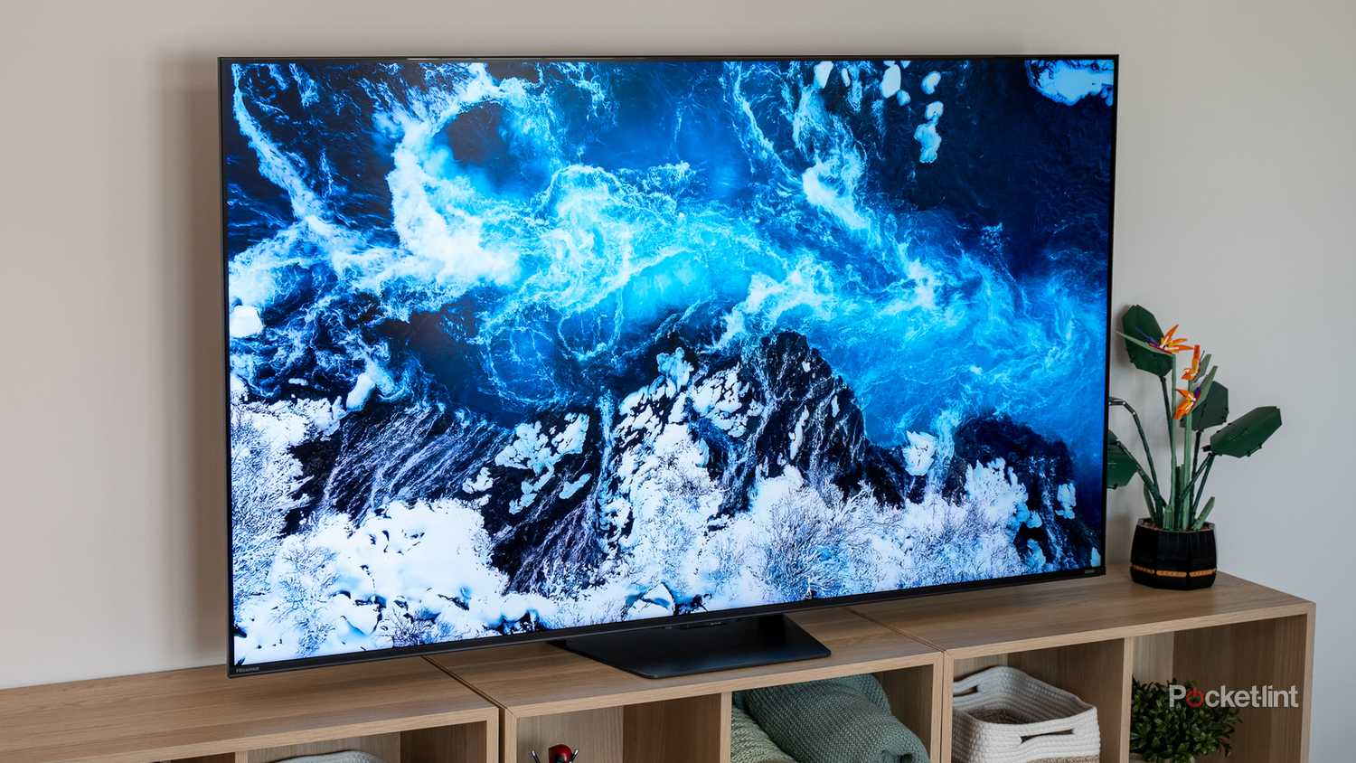 Hisense U7 TV on wood entertainment unit displaying an aerial view of ocean waves crashing over dark rocks.