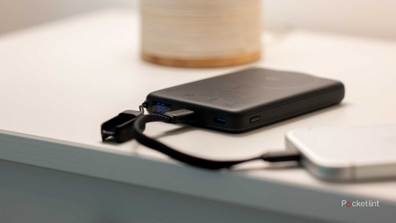 INIU SnapGo Air Power Bank on nightstand showing LED battery display with charging cable near lamp.