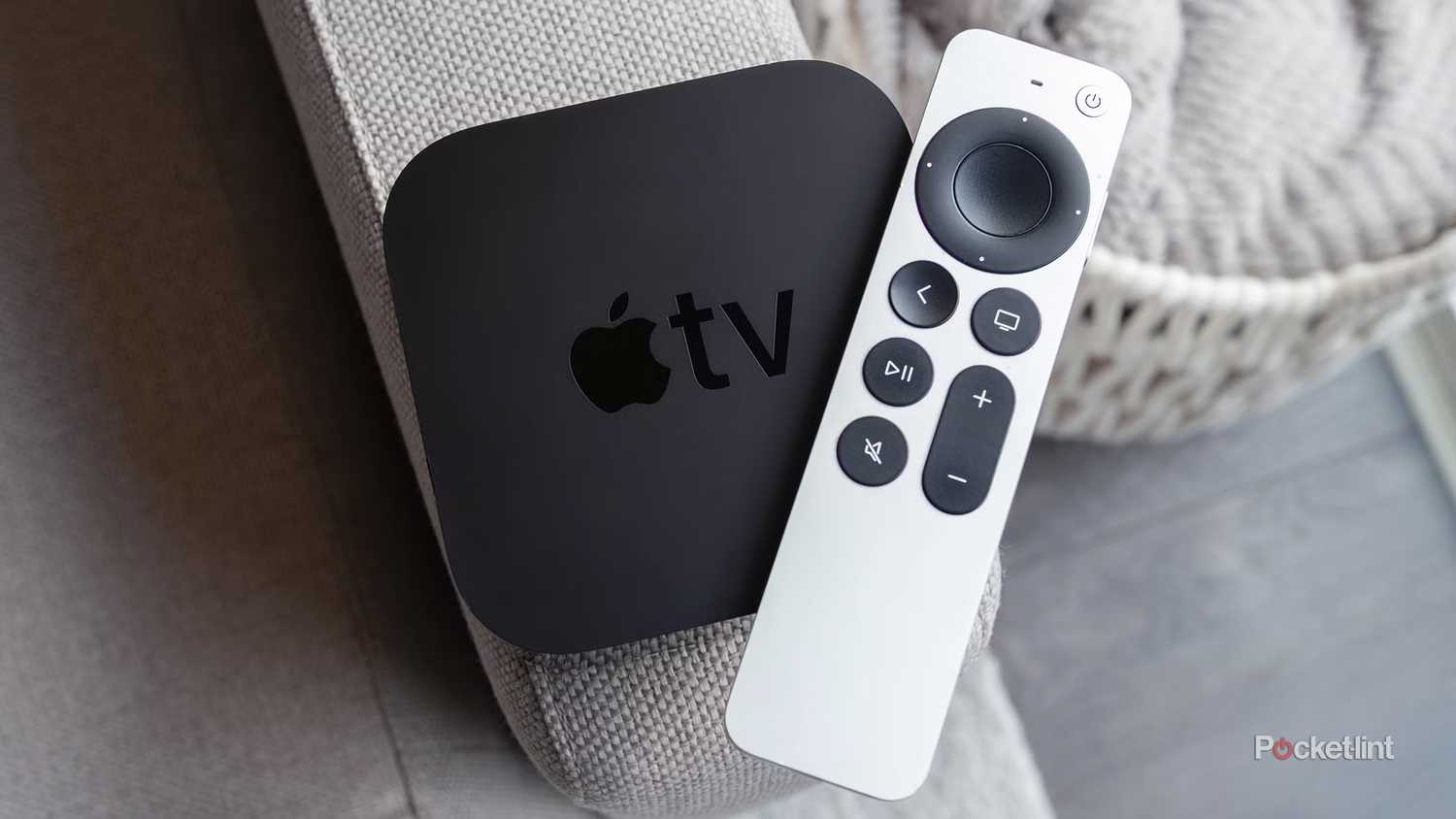 An Apple TV 4K and the Siri Remote sitting on a couch arm.