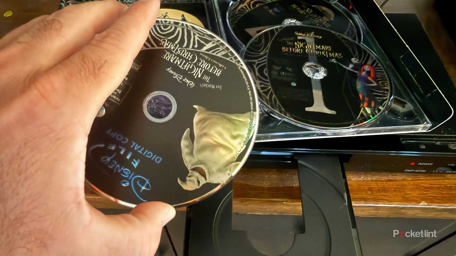 Hand holding Nightmare Before Christmas Blu-ray to insert it into Blu-ray player.