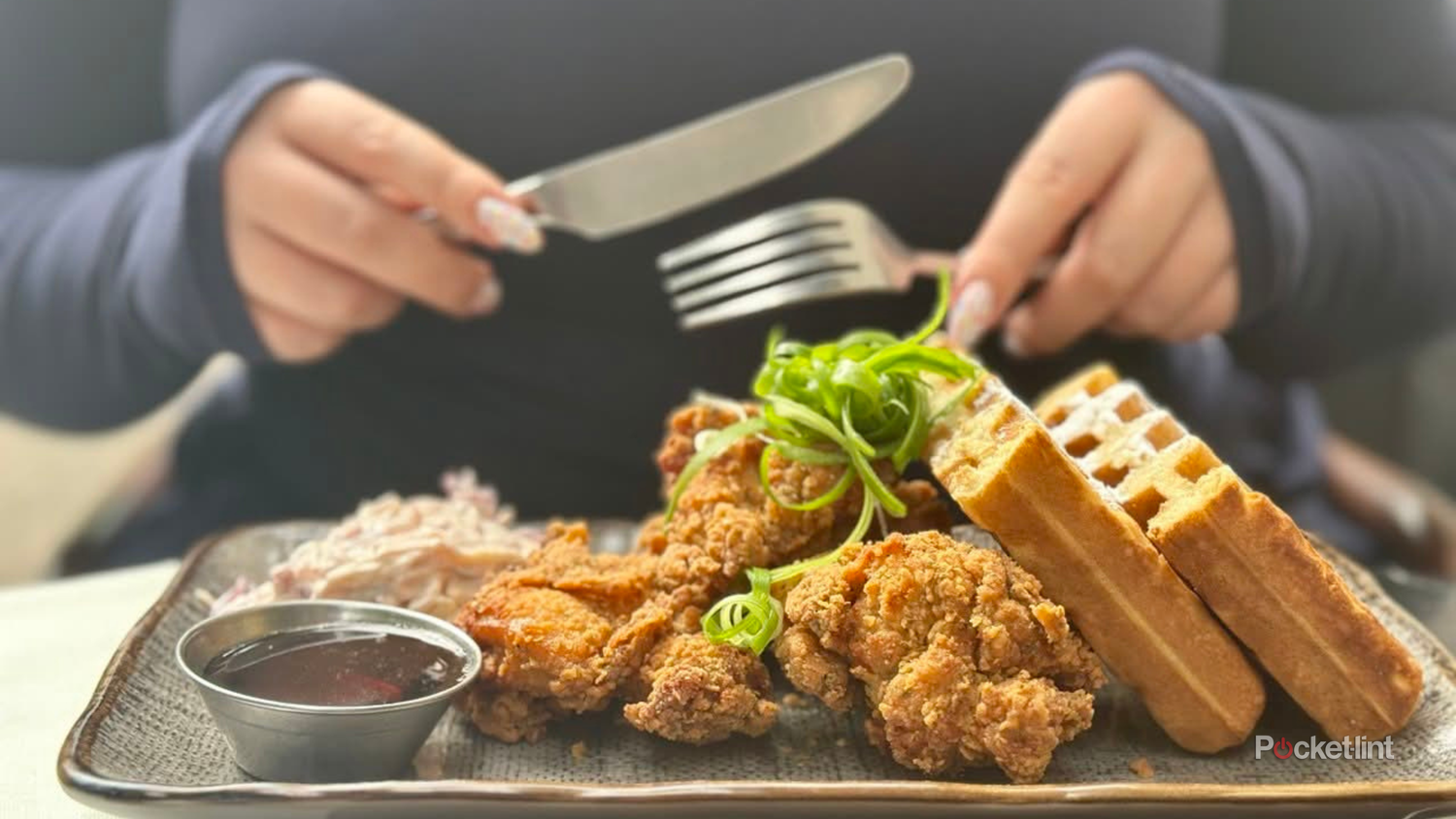 A woman cuts into a plate of fried chicken and waffles at an Amsterdam restaurant.