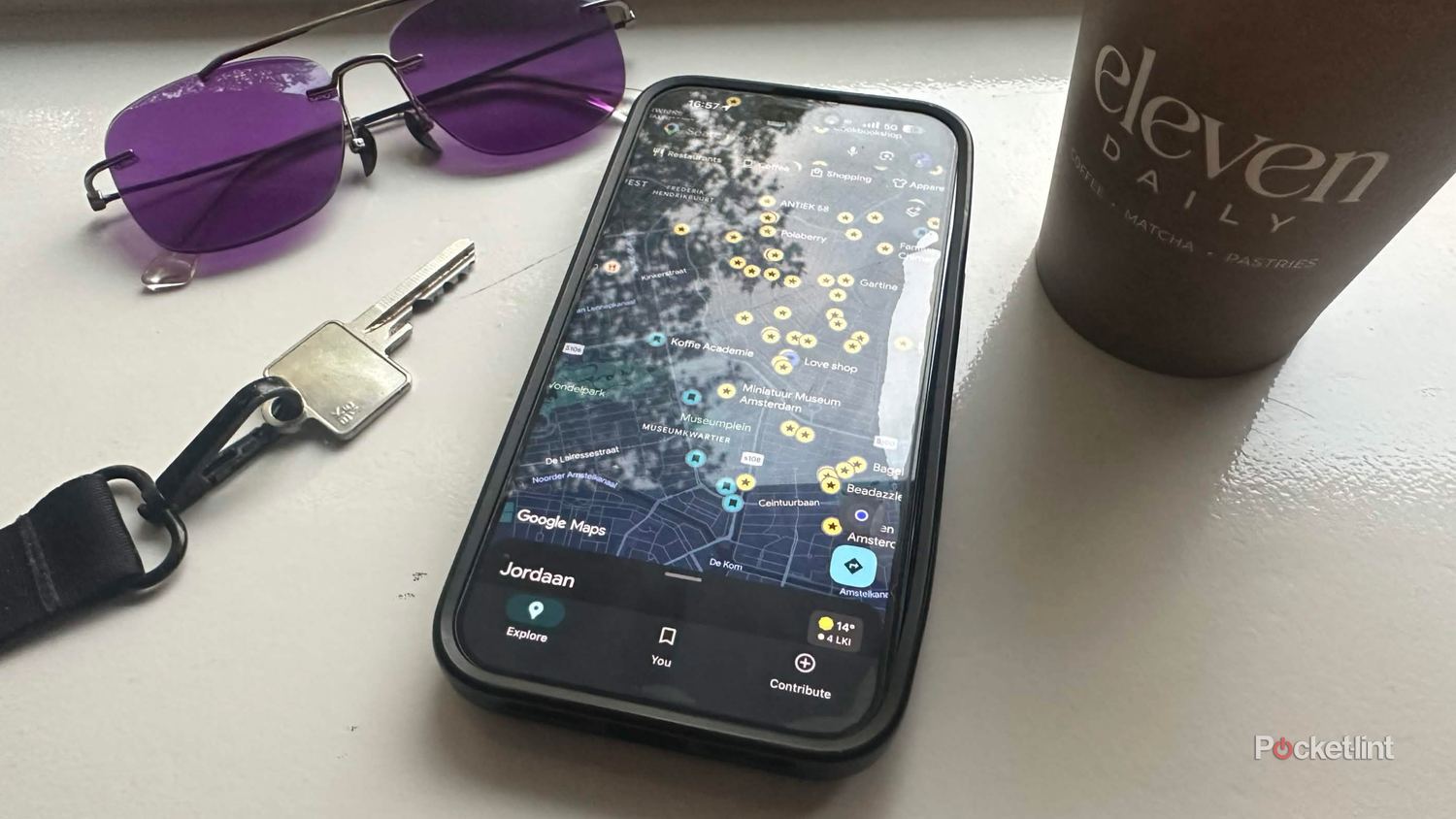 Google Maps showing saved places in Amsterdam beside keys, purple sunglasses, and a coffee.