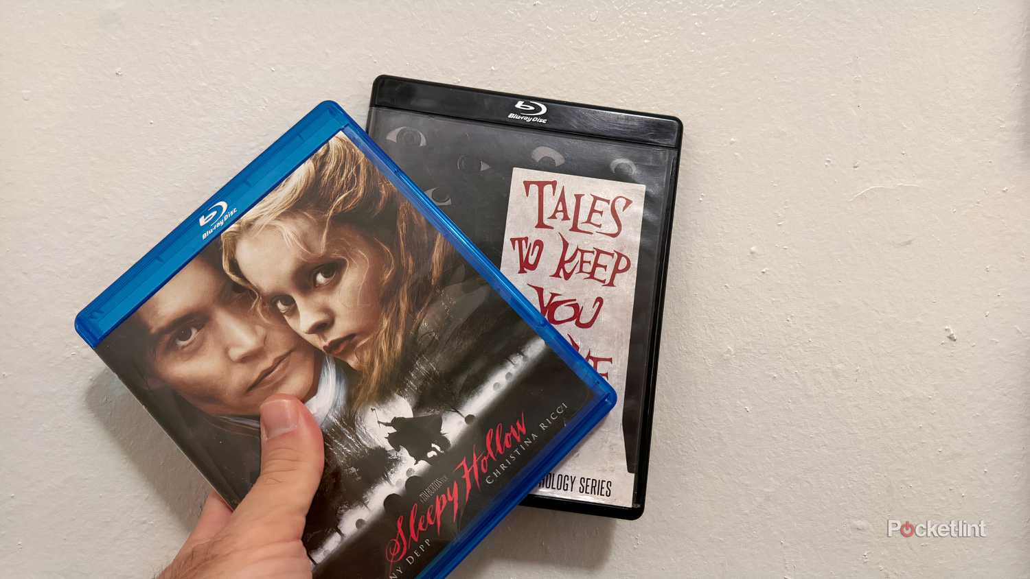 Blu-ray discs held in front of white wall.